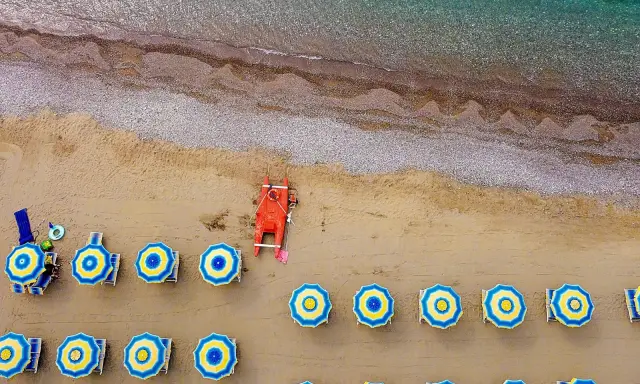 Ombrelloni blu e gialli e una barca rossa sulla spiaggia di Misano Marittima, con il mare turchese sullo sfondo.