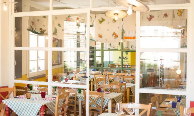 Interno di un'osteria de borg con tavoli apparecchiati con tovaglie a quadretti verdi e bianchi, sedie in legno e decorazioni colorate.