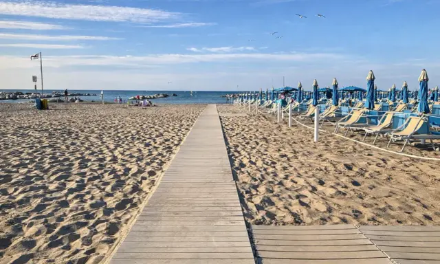 Passerella in legno sulla sabbia dorata di Rimini, con file di lettini e ombrelloni blu pronti per accogliere i bagnanti.