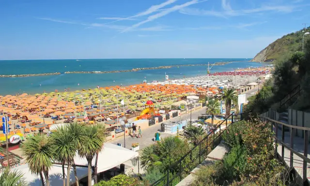 Ampia spiaggia libera a Gabicce Mare, con file infinite di ombrelloni colorati e lettini sotto un cielo azzurro.