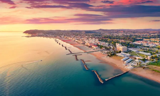 Alba rosa sul cattolica mare, con la costa e le colline sullo sfondo. Una barca solca le acque calme.