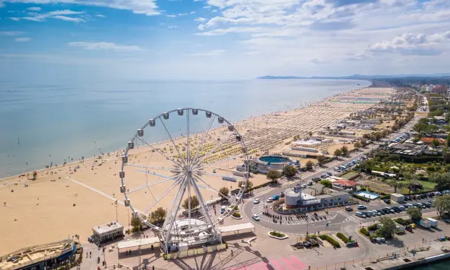 Vista aerea delle spiagge romagna con ruota panoramica, ombrelloni e mare azzurro.