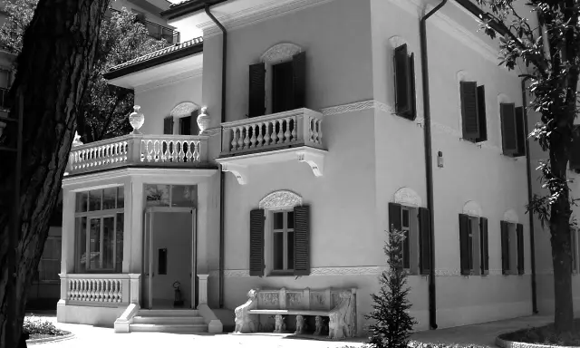 Villa Franceschi a Riccione, un'elegante dimora con balconi e un ingresso accogliente, circondata da alberi e un giardino curato.