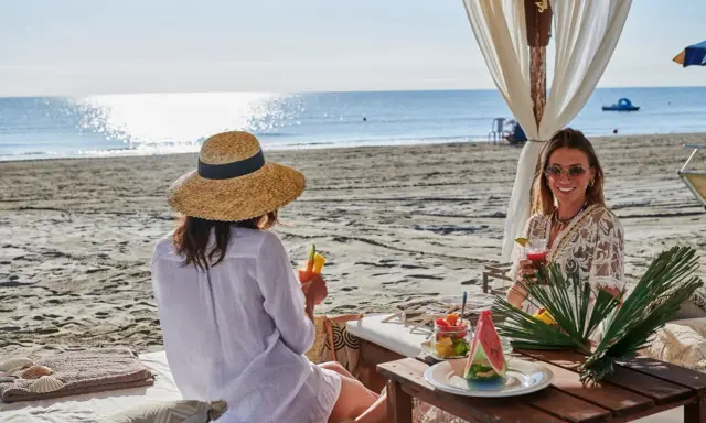 Due donne sorseggiano cocktail in un bagno Jacarè a Cervia, godendosi la spiaggia e il mare.