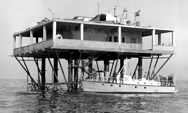 La struttura su palafitte, nota come Isola delle Rose, ospita persone su una barca ormeggiata.