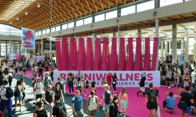 Folla animata a Rimini Wellness, un evento dedicato al benessere e al fitness. Persone di ogni età passeggiano tra gli stand e le aree espositive.