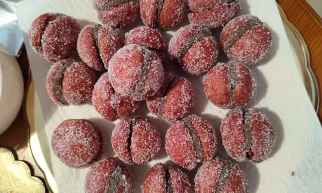 Dolci castagnole romagnole, due semisfere rosse unite da una crema scura e ricoperte di zucchero.