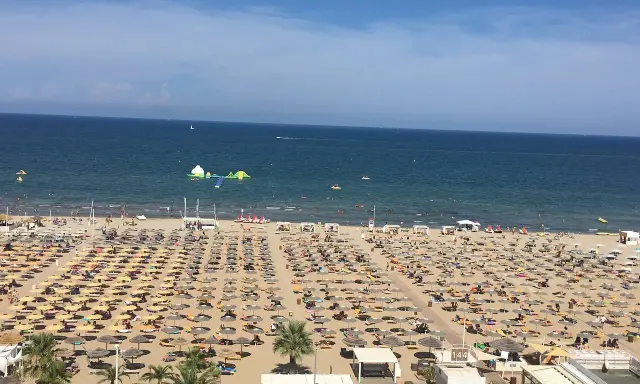 Una vasta spiaggia di Miramare gremita di ombrelloni e lettini, con bagnanti che si godono il sole e il mare azzurro.