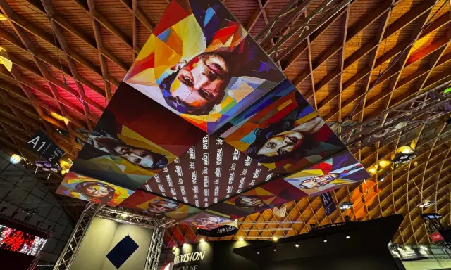 Installazioni artistiche colorate dominano il soffitto di una mir fiera, con volti stilizzati e il logo "Hikvision".