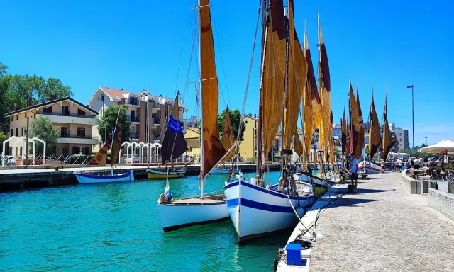Barche a vela ormeggiate in un porto con case colorate sullo sfondo. Un dilemma: meglio Bellaria o Igea Marina?