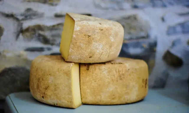 Formaggio Fossa stagionato, con crosta rustica e pasta gialla, impilato su uno sfondo di pietra grezza.