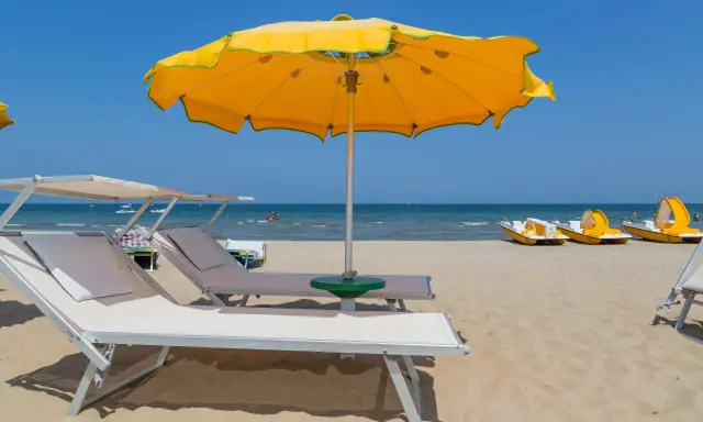 Spiagge di Rimini con lettini, ombrellone giallo e pedalò pronti per l'estate.