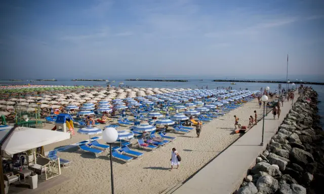 Spiaggia affollata a Gatteo Mare centro, con file di ombrelloni e lettini, gente che passeggia sul molo e si gode il sole.