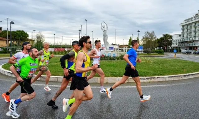 Atleti impegnati nella Rimini Half Marathon, corrono su asfalto bagnato con un cielo nuvoloso.