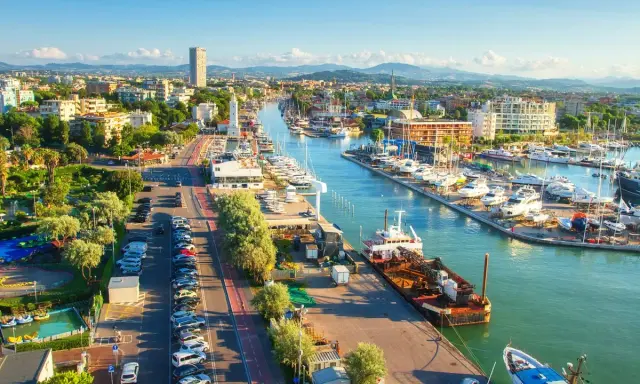 Vista aerea di un vivace **club nautico** con barche ormeggiate, edifici moderni e un faro bianco.