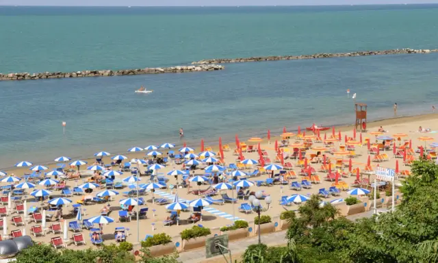 Spiaggia affollata con ombrelloni colorati, lettini e bagnanti. Perfetta idea per sapere dove andare al mare in Emilia Romagna.