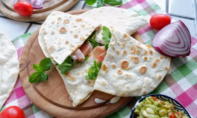 Piadina, piatto tipico di Rimini, farcita con prosciutto e rucola, servita con guacamole e verdure fresche.
