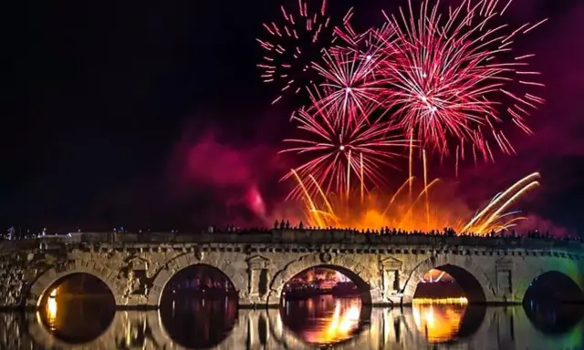 Fuochi d'artificio spettacolari illuminano il cielo notturno sopra un ponte storico, celebrando il capodanno in riviera romagnola.