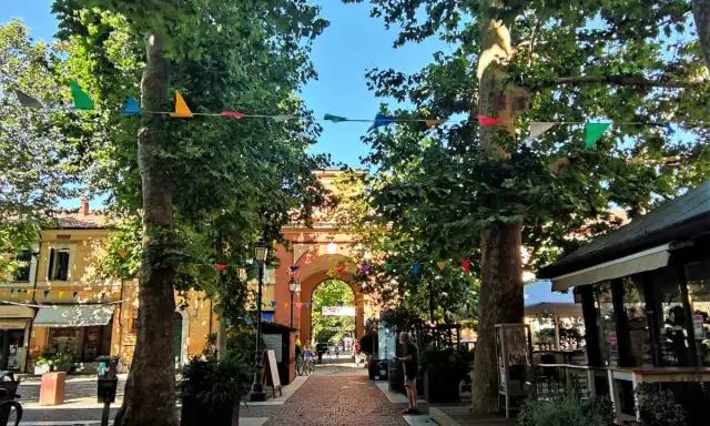 V Cervia centro, un viale alberato con festoni colorati conduce a un arco monumentale.