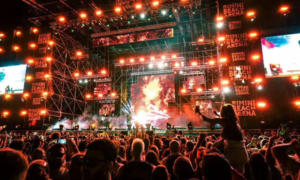 Un concerto elettrizzante alla Rimini Beach Arena. Migliaia di fan in delirio sotto un palco imponente illuminato da luci stroboscopiche e schermi giganti.