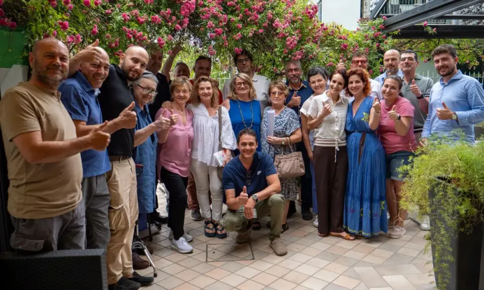 Un gruppo di persone sorridenti festeggia la primavera viserba sotto un pergolato fiorito.