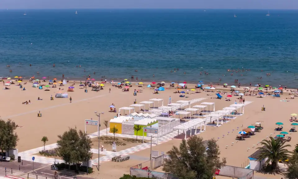 Una vivace spiaggia libera a Rimini, con bagnanti che si godono il sole e il mare sotto ombrelloni colorati.