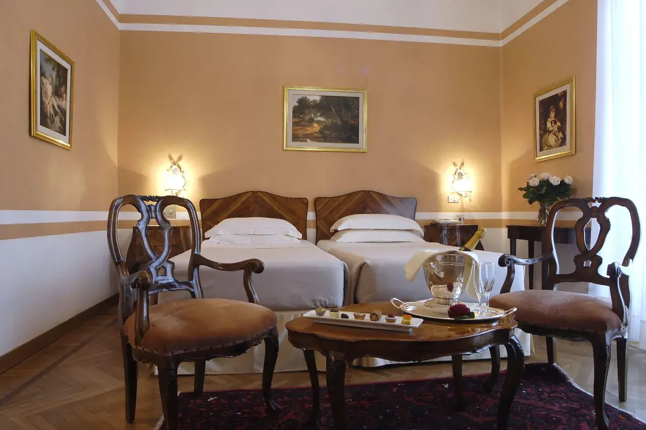 Camera elegante con due letti singoli, un tavolino con champagne e pasticcini, e sedie d'epoca. Un assaggio di lusso al Grand Hotel Rimini.