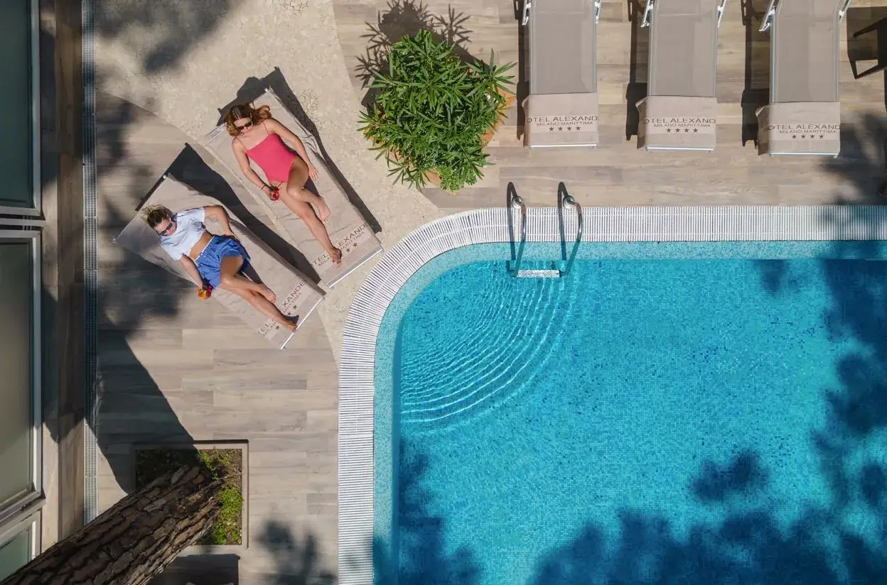 Due donne rilassate a bordo della piscina di Milano Marittima, con lettini e ombrelloni.