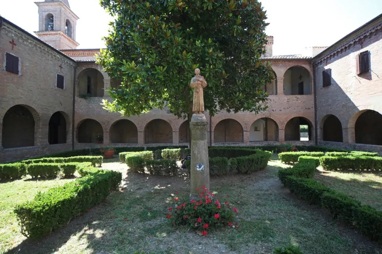 Cortile di una villa a Verucchio con statue, alberi e siepi curate.