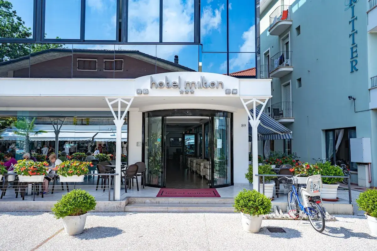 Ingresso accogliente dell'Hotel Milton Valverde con tavolini all'aperto e fiori colorati. Biciclette parcheggiate, pronte per esplorare.