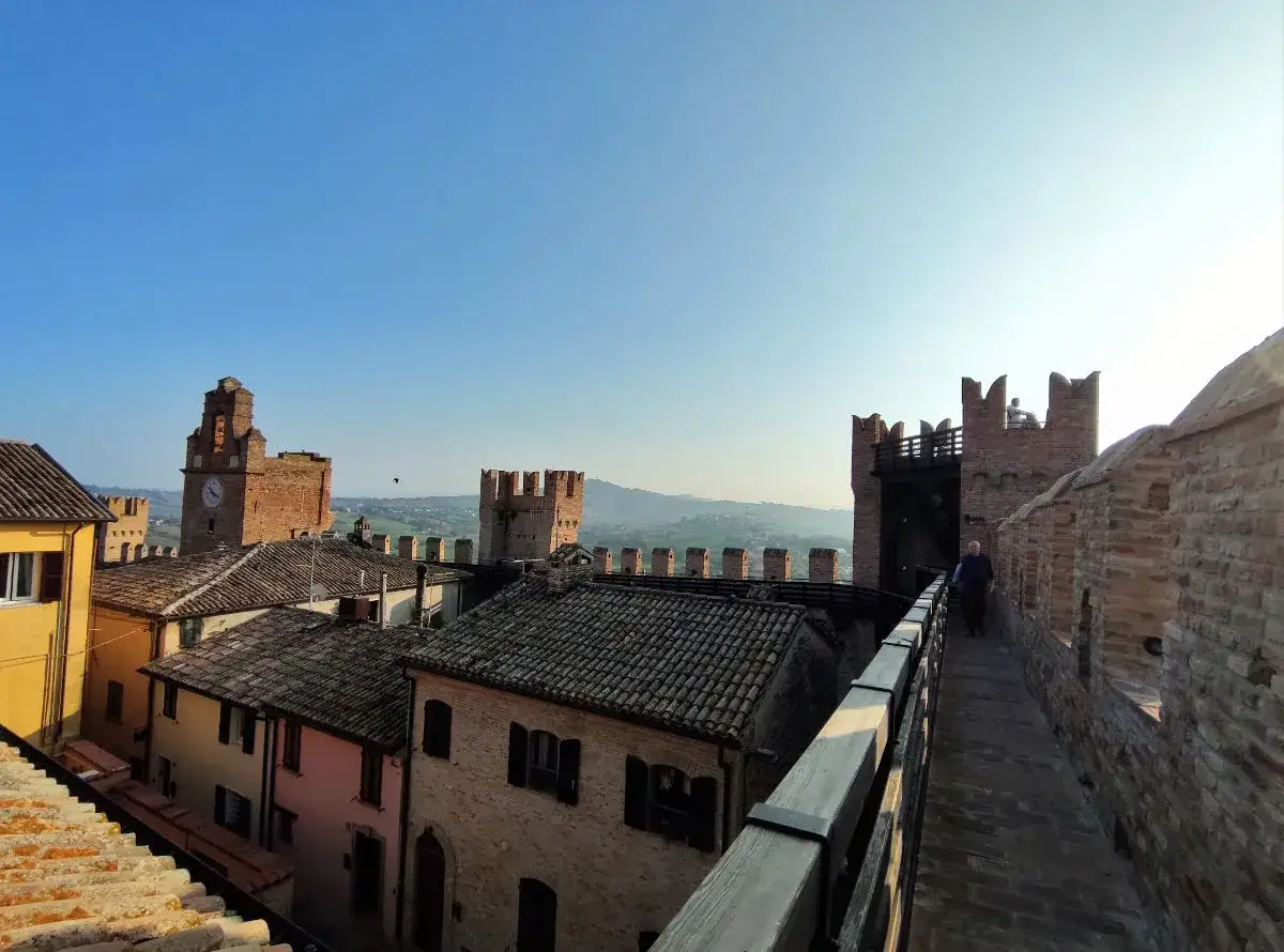 Passeggiata sulle mura del castello di Gradara, con vista sui tetti e le torri medievali.
