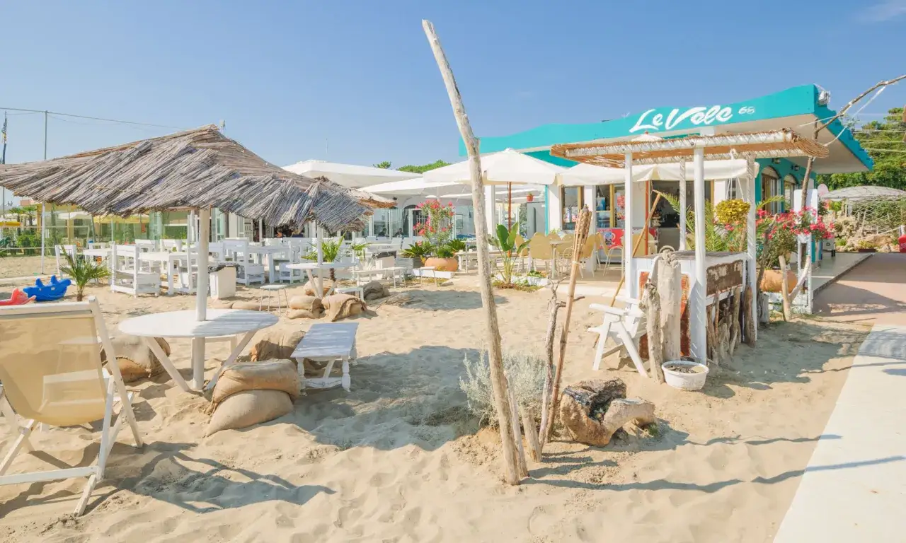 Stabilimenti balneari Cervia: tavoli e sedie bianche sotto ombrelloni di paglia e tende, con il bar 