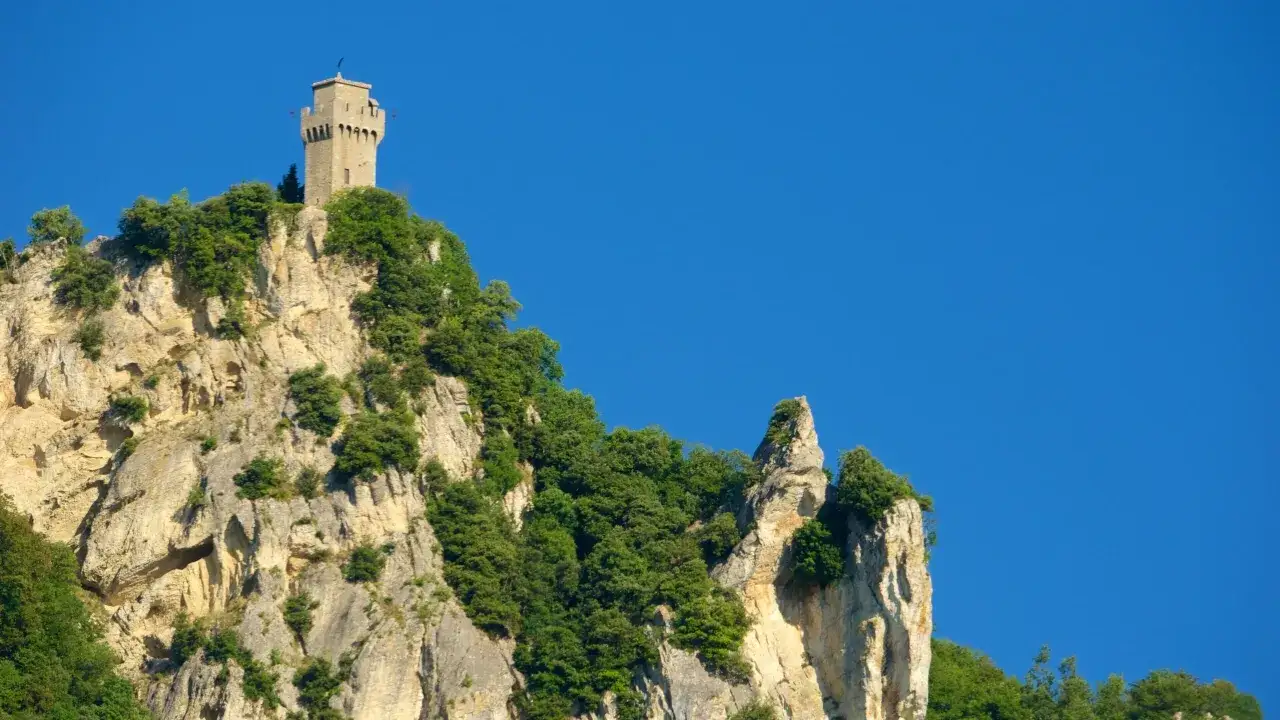 Torre medievale su una roccia scoscesa, parte del San Marino castle, con vegetazione rigogliosa e cielo azzurro.