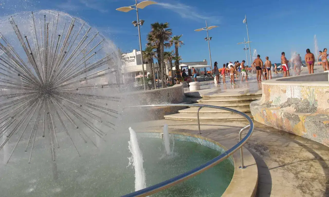 Fontana a forma di dente di leone e persone che si rinfrescano in una giornata di sole a Misano Adriatico centro.