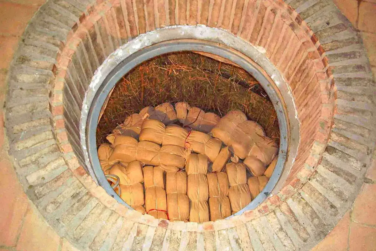 Pacchi di formaggio fossa, avvolti in tela e legati con spago, riposano in una fossa circolare in mattoni, coperta da paglia.