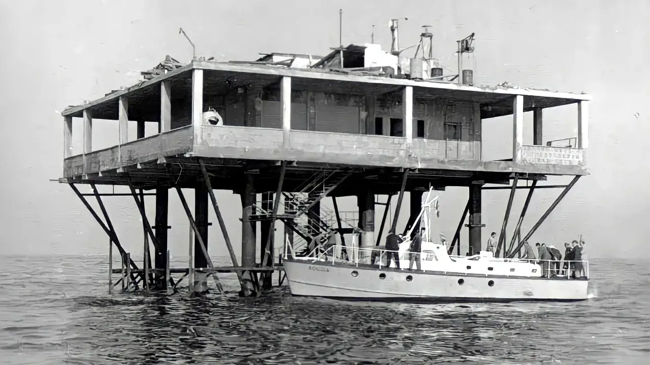 La struttura su palafitte, nota come Isola delle Rose, ospita persone su una barca ormeggiata.
