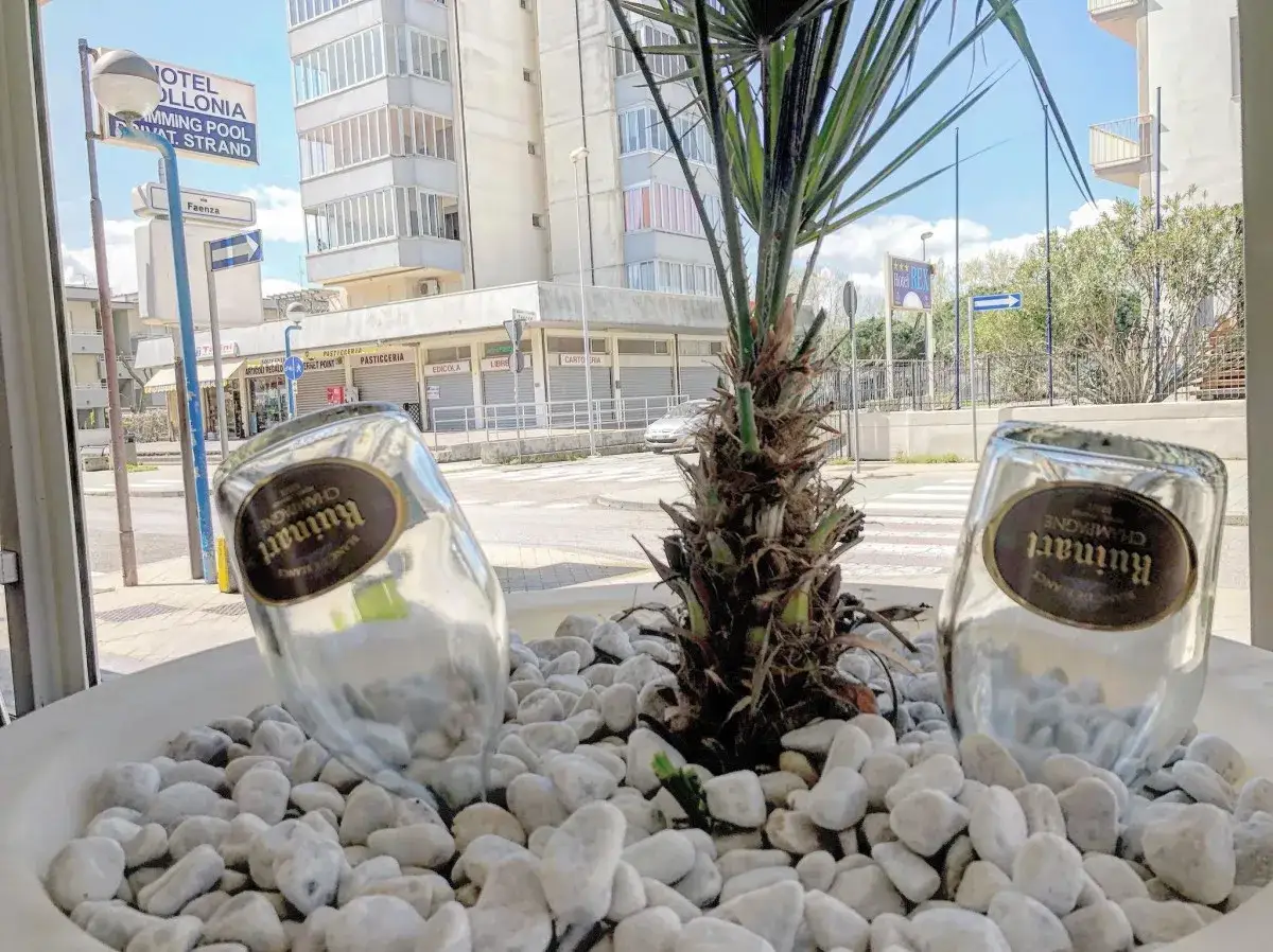 Bottiglie di champagne Ruinart in un vaso con ciottoli bianchi, davanti a un bar lido di Savio.