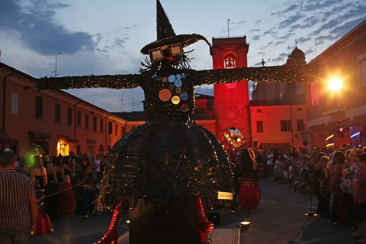 Un'enorme strega di pezza domina la piazza, circondata da una folla festante. È la notte delle streghe, un evento magico e suggestivo.