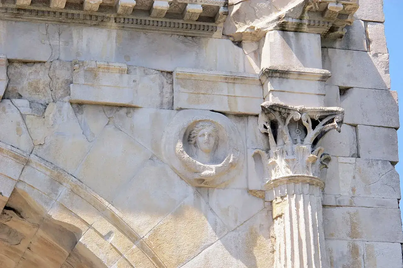 Dettaglio dell'arco d'Augusto a Rimini: un volto femminile scolpito in un tondo, con un capitello corinzio a destra.