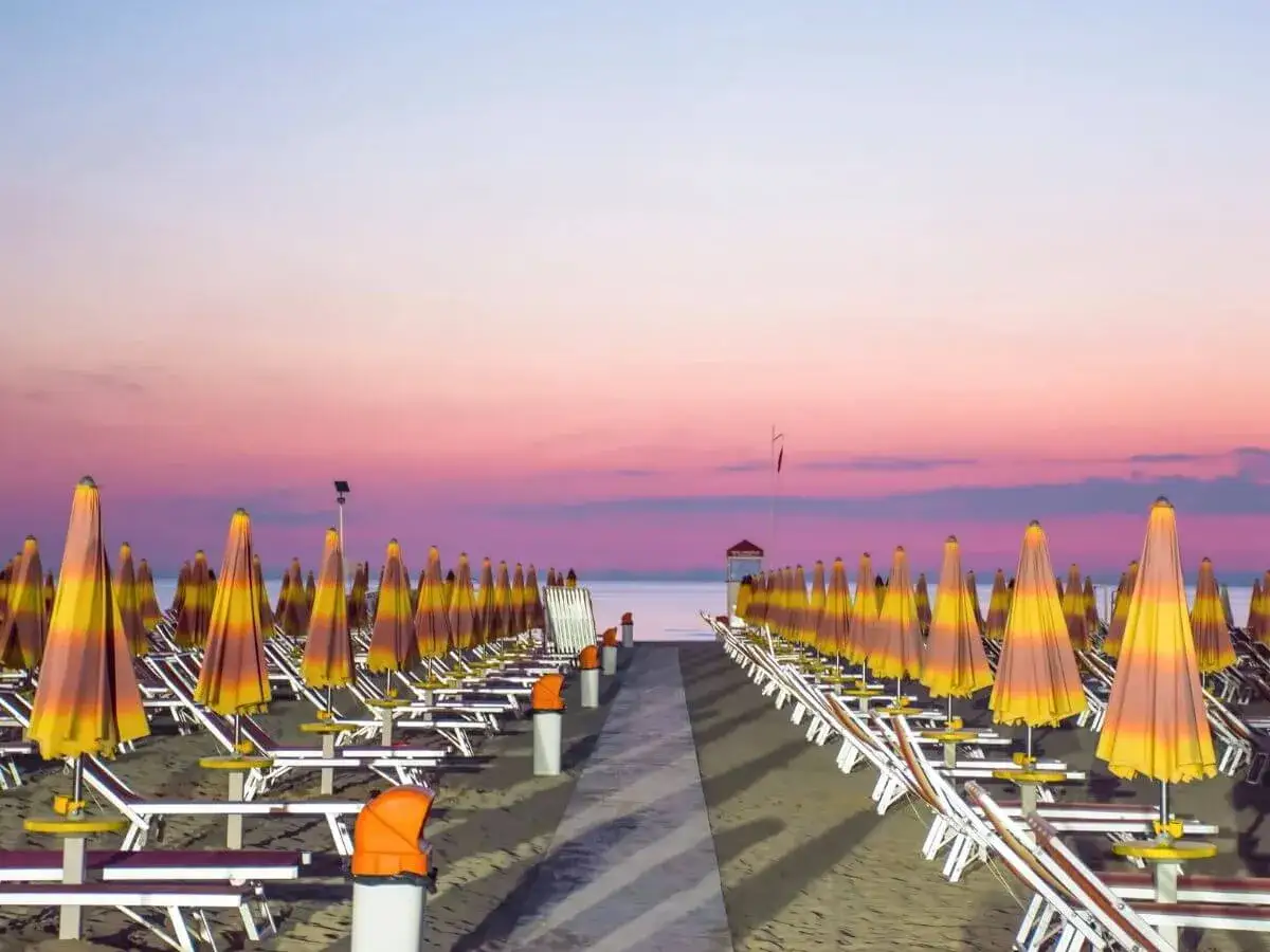 Filettate di ombrelloni e lettini sulla spiaggia di Riccione al tramonto. Un invito a scoprire cosa fare a Riccione.
