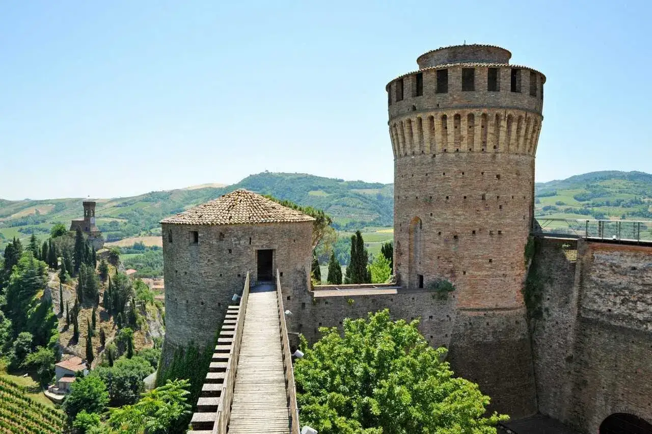 Rocche e torri medievali, tra i paesi belli vicino Ravenna, dominano colline verdi e vigneti sotto un cielo azzurro.