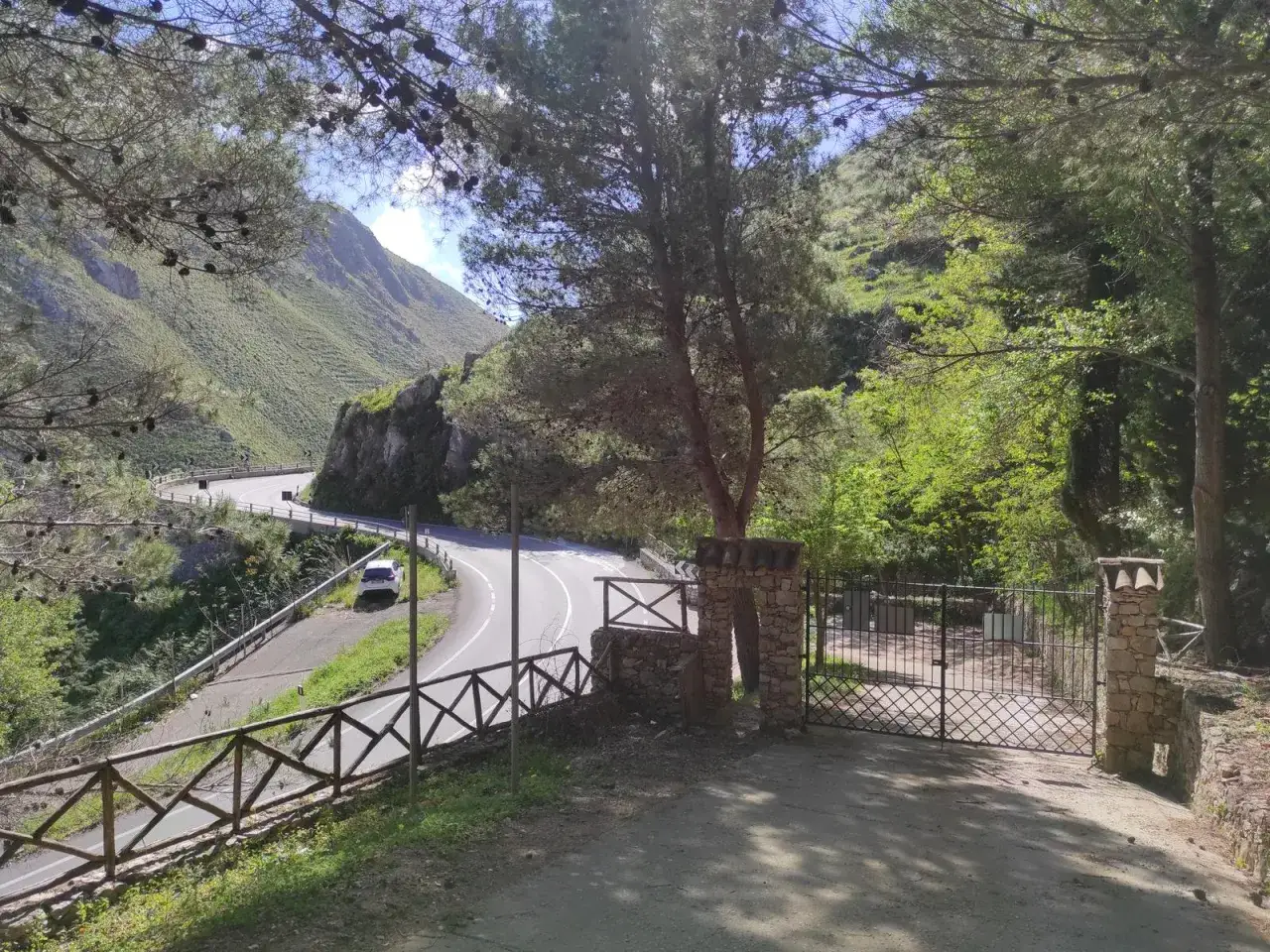 Strada tortuosa sul monte Gradara, con un'auto bianca parcheggiata e un cancello in pietra.