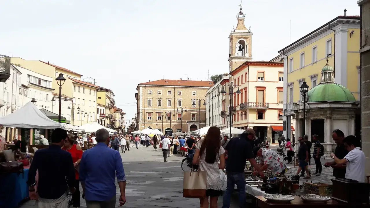 Gente passeggia tra bancarelle e palazzi storici, un vivace mercatino usato a Rimini.