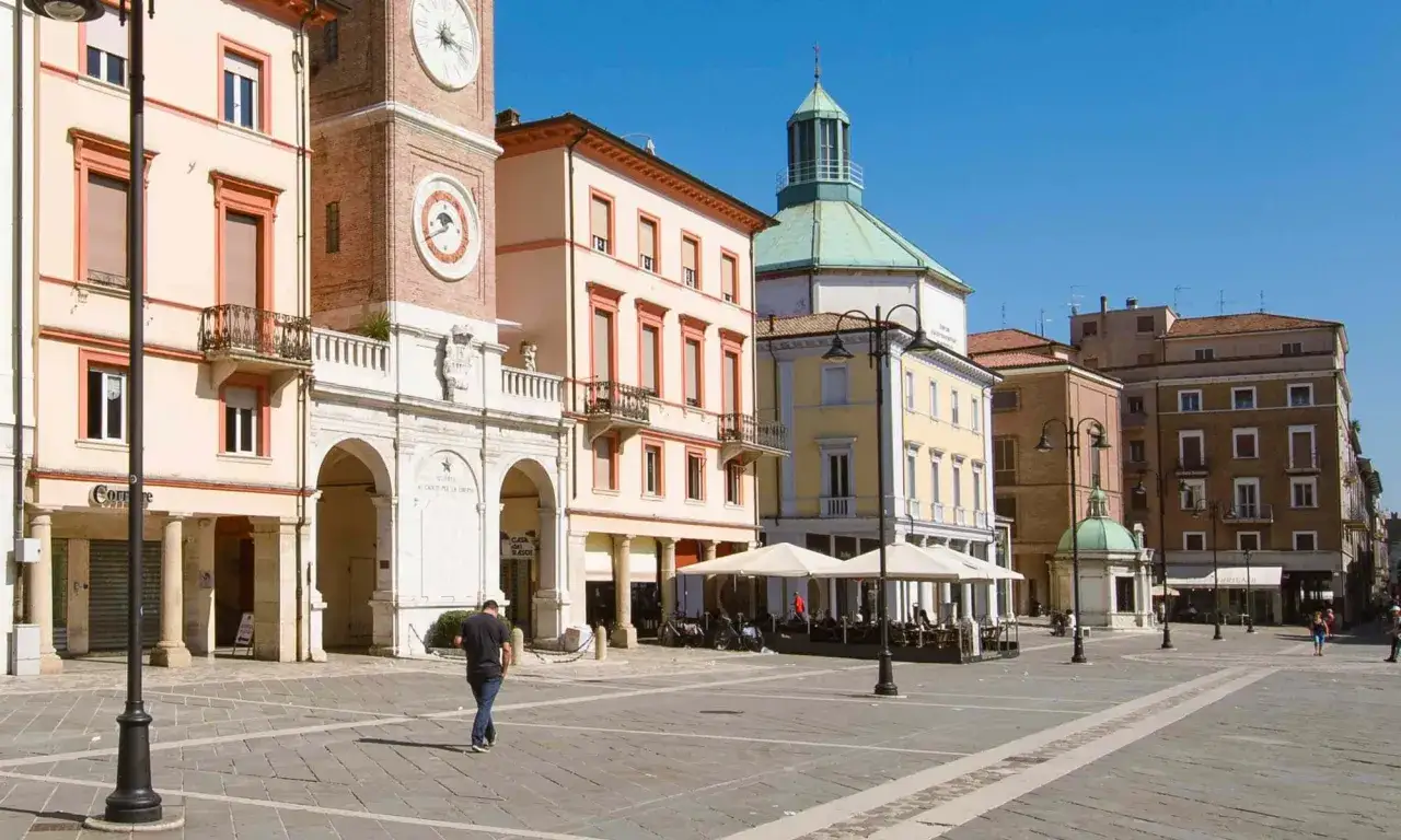 Passeggiata nella soleggiata piazza Tre Martiri a Rimini, con i suoi palazzi storici e un caffè all'aperto.