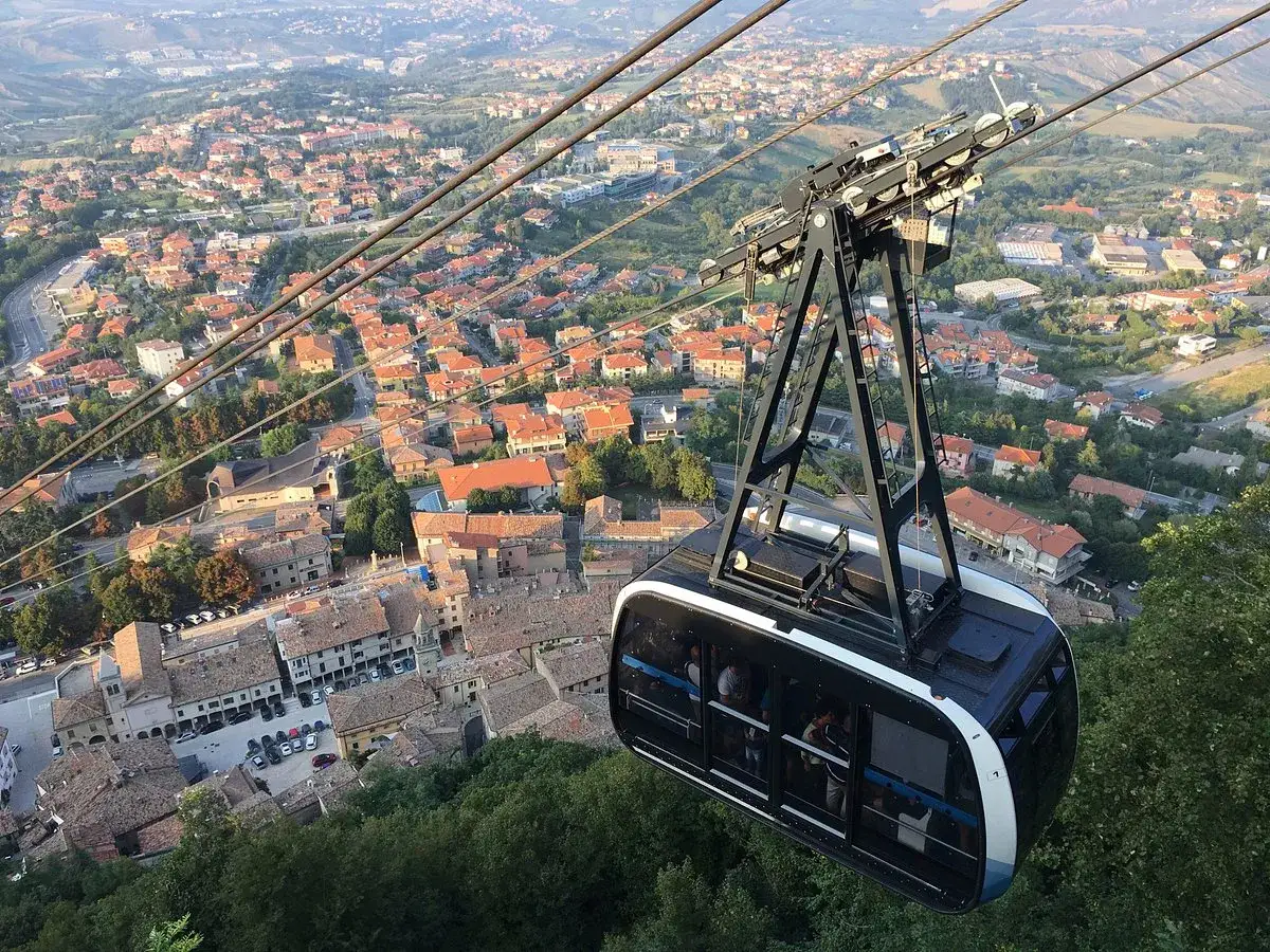 Cabina della funivia di San Marino in volo, con vista panoramica sulla città e sui tetti rossi.