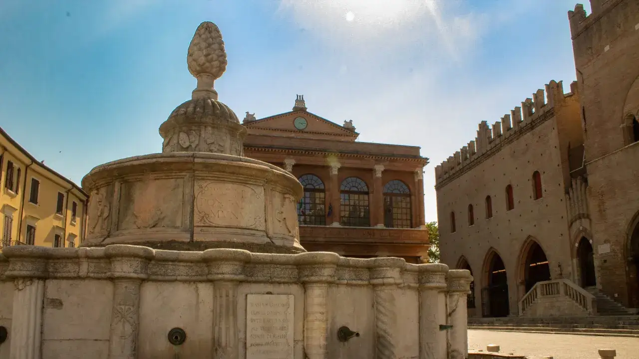 Fontana storica e palazzi medievali nella rimini altstadt, sotto un cielo azzurro.