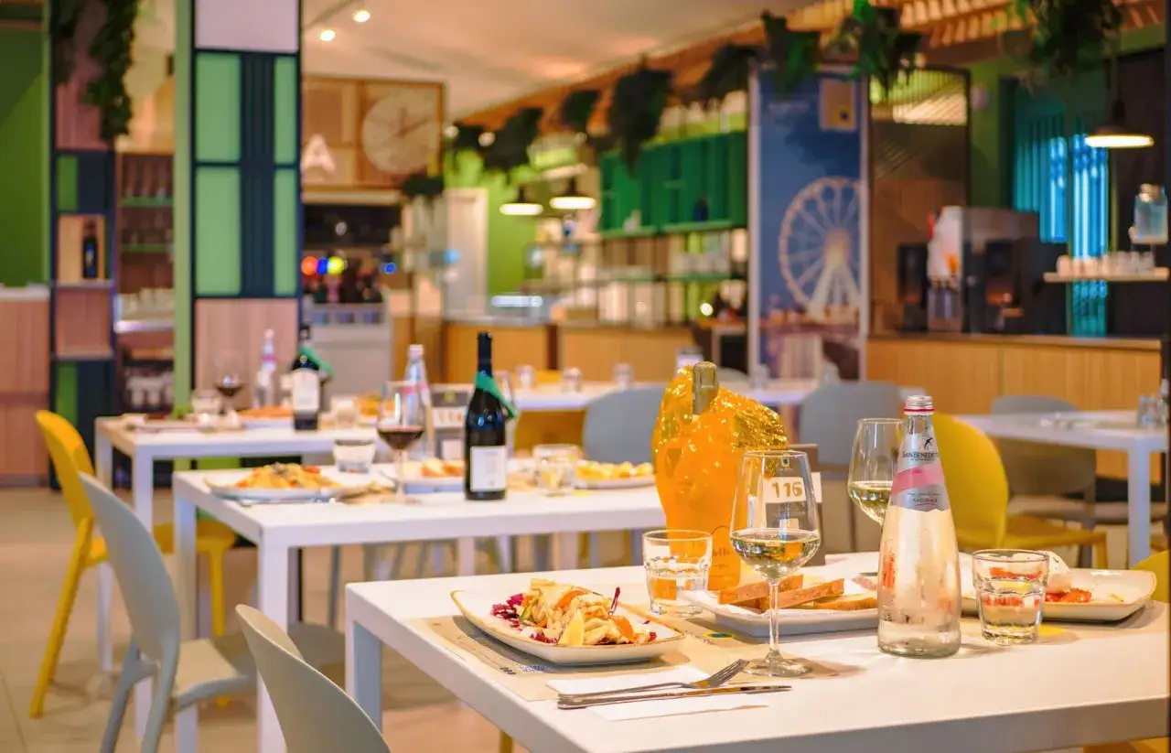 Tavoli apparecchiati in un locale moderno, con bottiglie di vino e piatti invitanti. L'atmosfera suggerisce un'esperienza culinaria di alto livello, forse il miglior ristorante di Rimini.