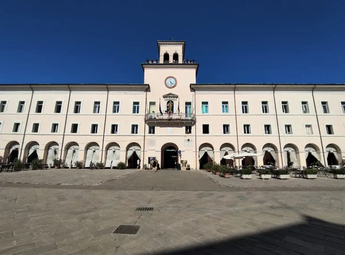 Piazza del Popolo a Cervia centro, con il Palazzo Comunale color pesca e il suo orologio. Tavolini all'aperto invitano a una pausa.