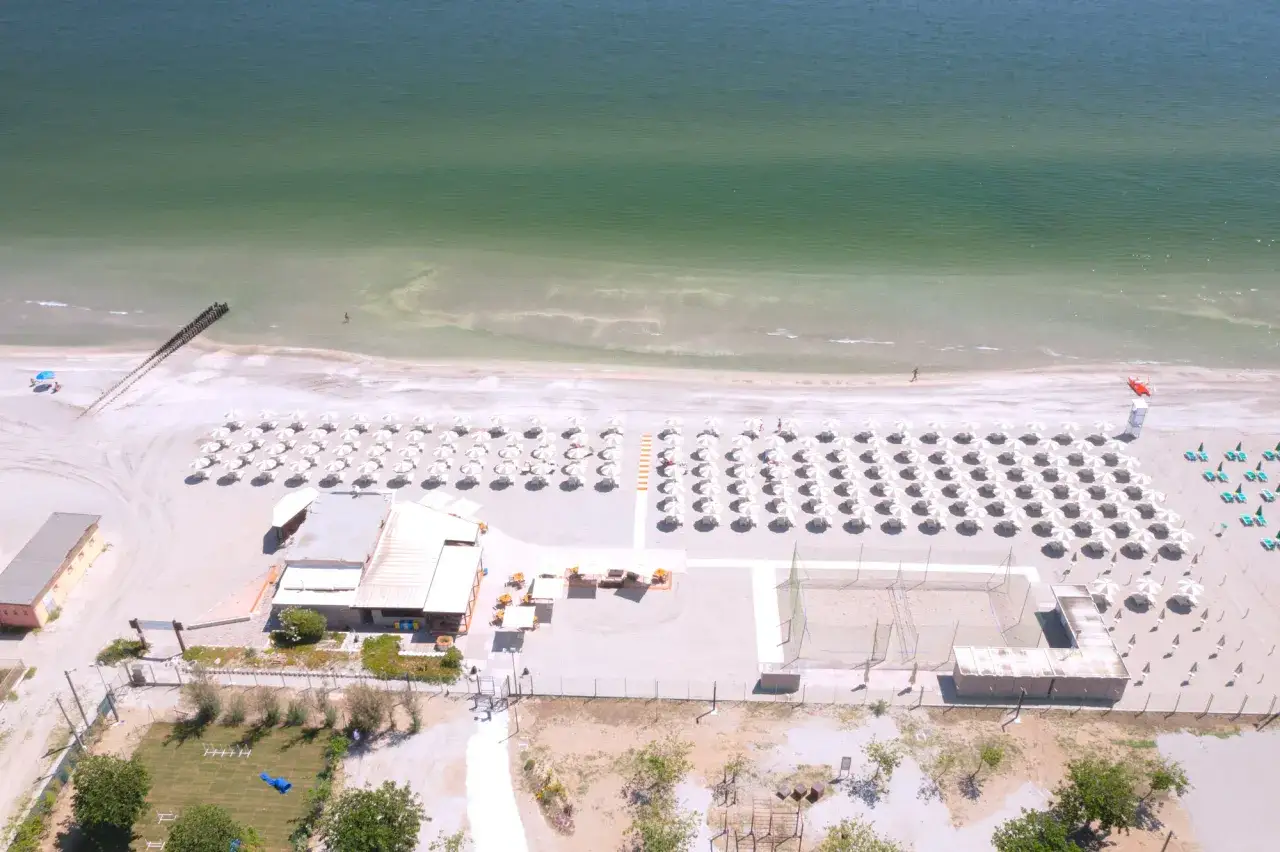 Spiaggia ordinata a Milano Marittima con file di ombrelloni bianchi, lettini, un campo da beach volley e il mare verde.