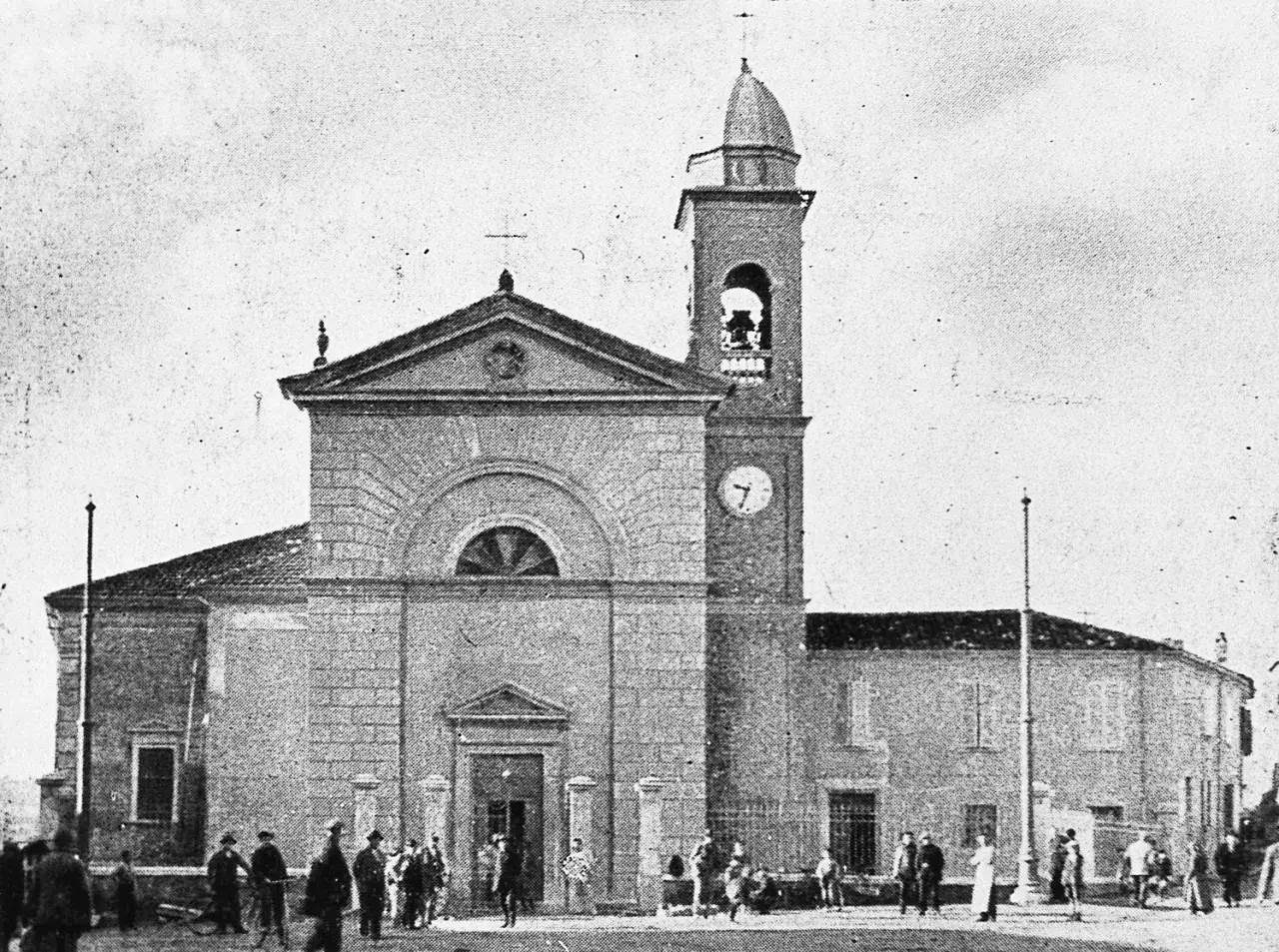 La chiesa di San Gaudenzio a Rimini, con la sua torre campanaria e l'orologio. Persone passeggiano davanti.